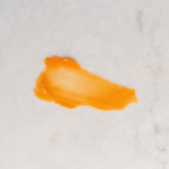 A textured smear of bright orange colored Bowellia & Rose Eye Balm on a light gray marble surface.