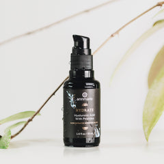 Hydrate Hyaluronic Acid with Peptides concentrated boosting elixir in a dark glass pump bottle with water droplets, styled with green leaves.
