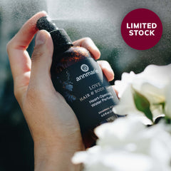 Hand holding a bottle of Love Hair & Body Mist with flowers in the background and 'LIMITED STOCK' label.